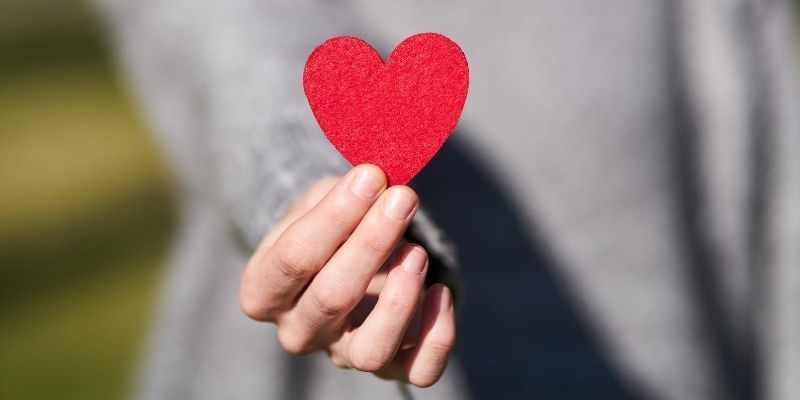 Self-compassion survey - young woman's hand offering a paper heart